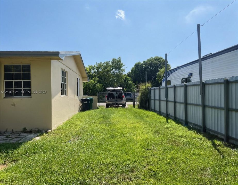 Exterior space featuring a grass yard, perimeter metal fencing, and a side-mounted windowed structure