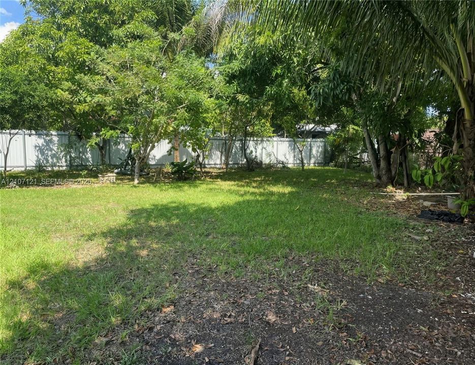 Backyard featuring a grass lawn, metal perimeter fencing, and mature trees
