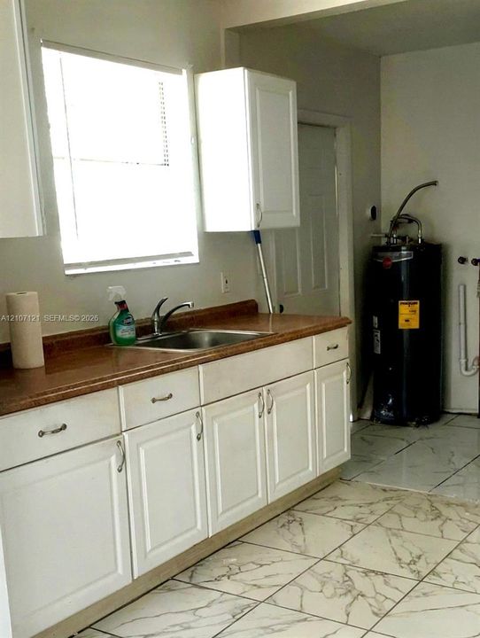 White shaker-style cabinetry, solid-surface countertop, stainless steel undermount sink with chrome faucet, and large-format tile flooring