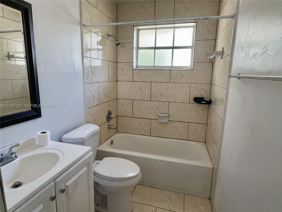 Bathroom featuring a white vanity cabinet, ceramic tile tub surround, integrated porcelain sink, and a window with a muntin grid