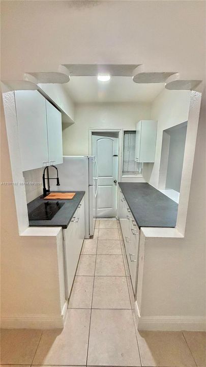 Kitchen featuring white cabinetry, dark countertops, a matte black faucet, a built-in cooktop, and tile flooring