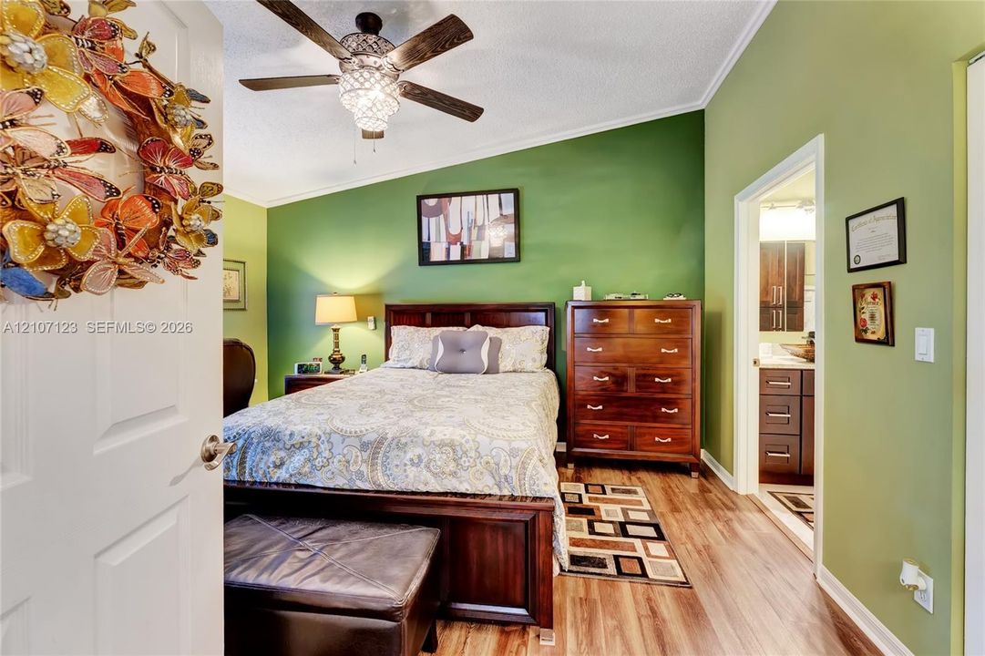 Sloped ceiling featuring a multi-blade ceiling fan with an integrated light fixture and wood-finish flooring