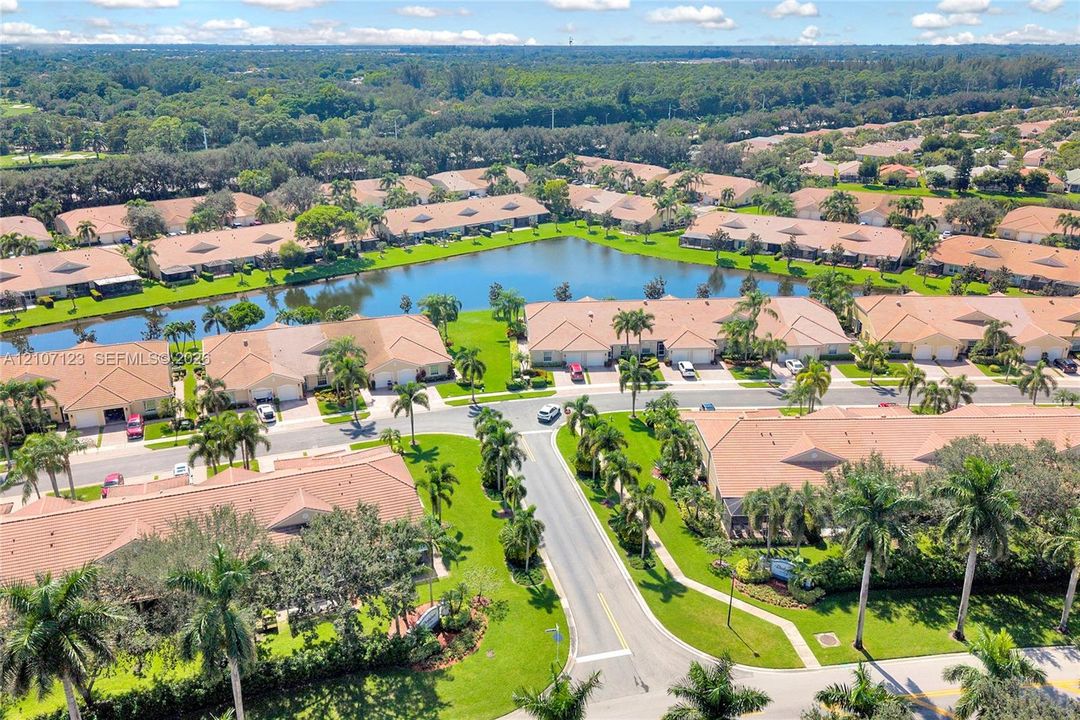 Aerial perspective of a residential community featuring a central lake, manicured lawns, mature palm trees, and paved street infrastructure