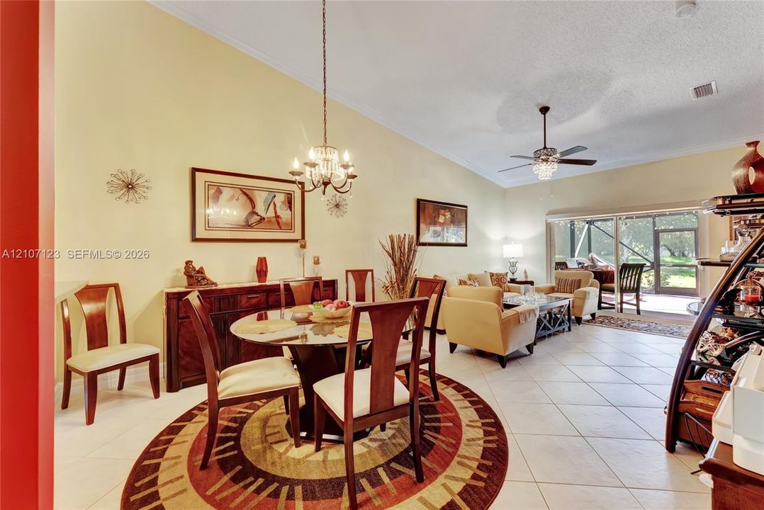 Vaulted ceilings featuring a chandelier, tile flooring, and sliding glass doors with a screen enclosure