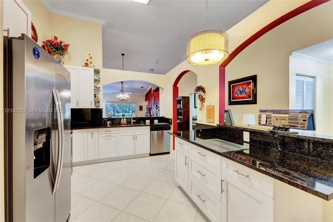 Kitchen featuring white shaker-style cabinetry, dark stone countertops, stainless steel appliances, tile flooring, and arched architectural detailing