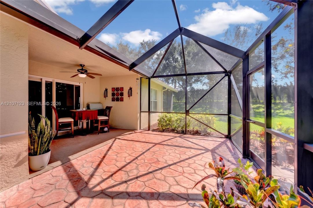 Screened-in lanai featuring a stamped concrete patio, vaulted structural framing, and a mounted ceiling fan