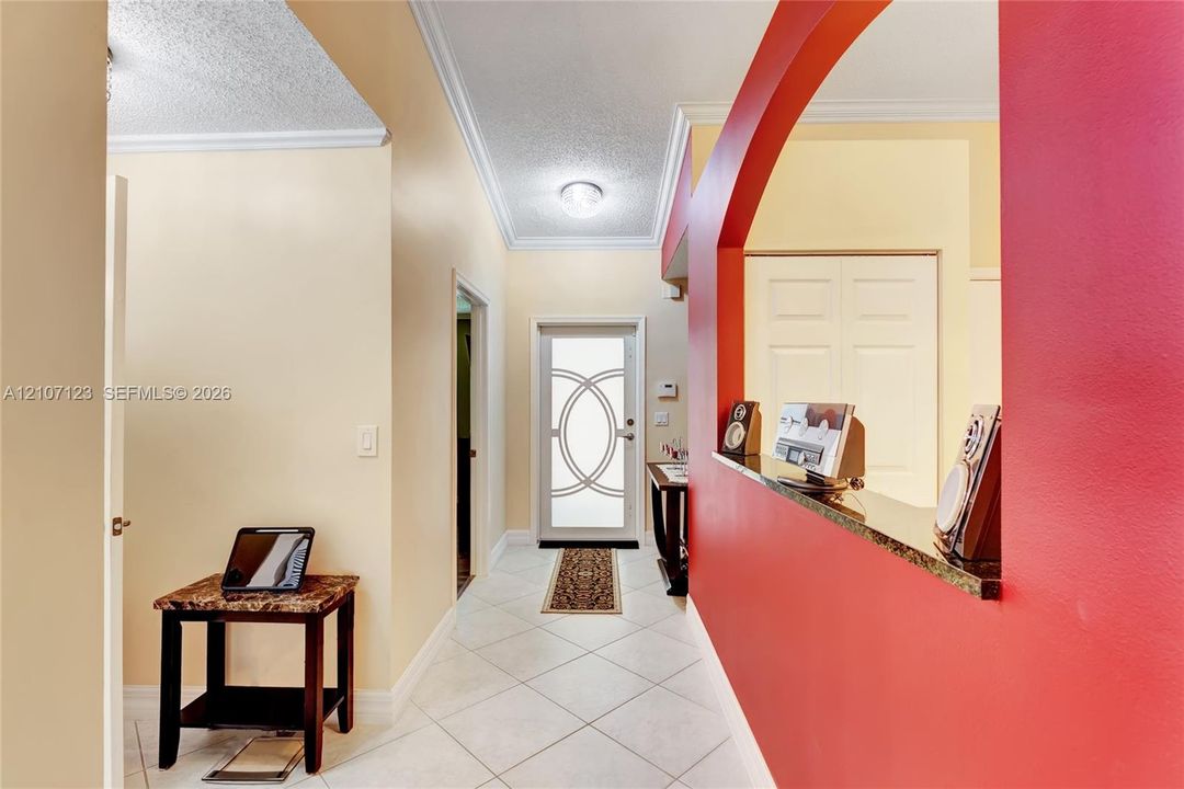 Entryway featuring ceramic tile flooring, a glass-paneled front door, an arched wall cutout with a solid surface pass-through, and double-door closet cabinetry