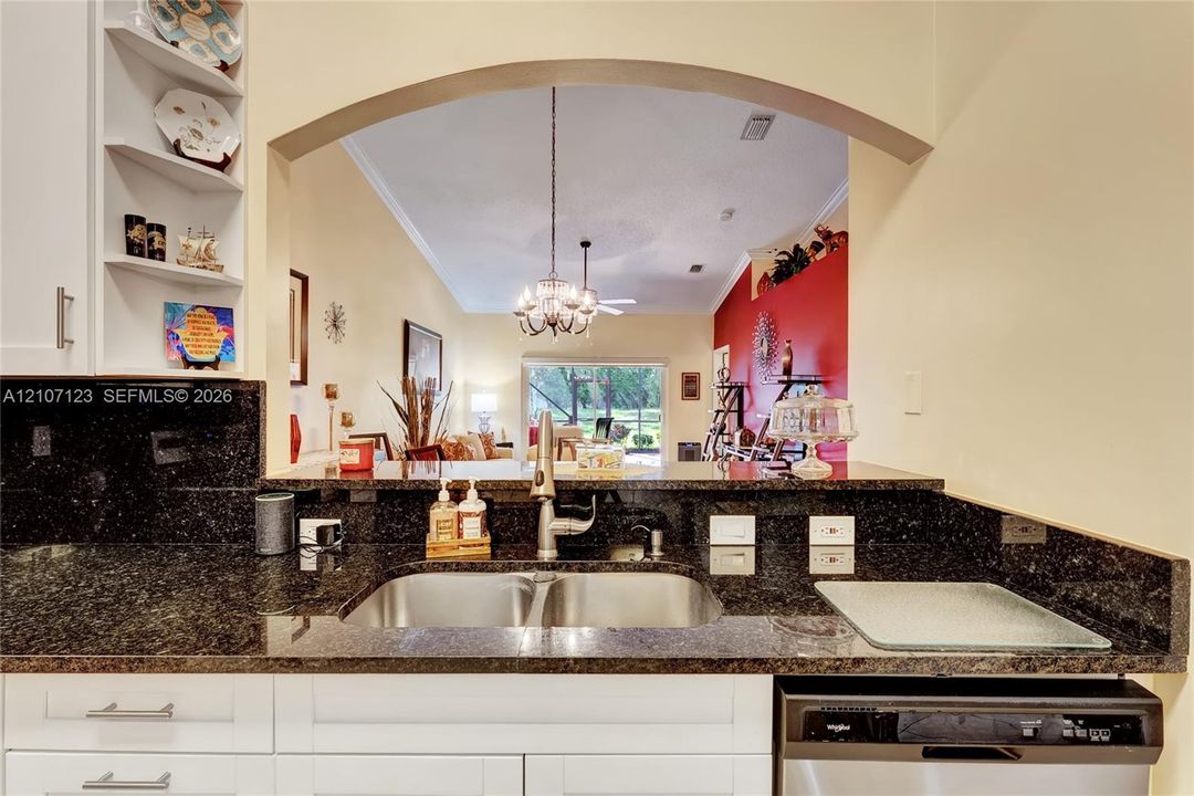 Kitchen featuring white cabinetry, dark stone countertops, an arched service window, double-basin stainless steel sink with a high-arc faucet, and an integrated stainless steel dishwasher