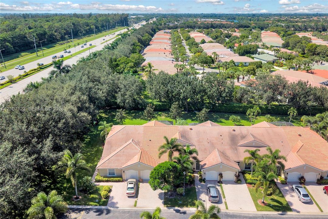 Aerial perspective of a multi-unit residential building featuring a tile roof, concrete driveways, and mature landscaping with palm trees
