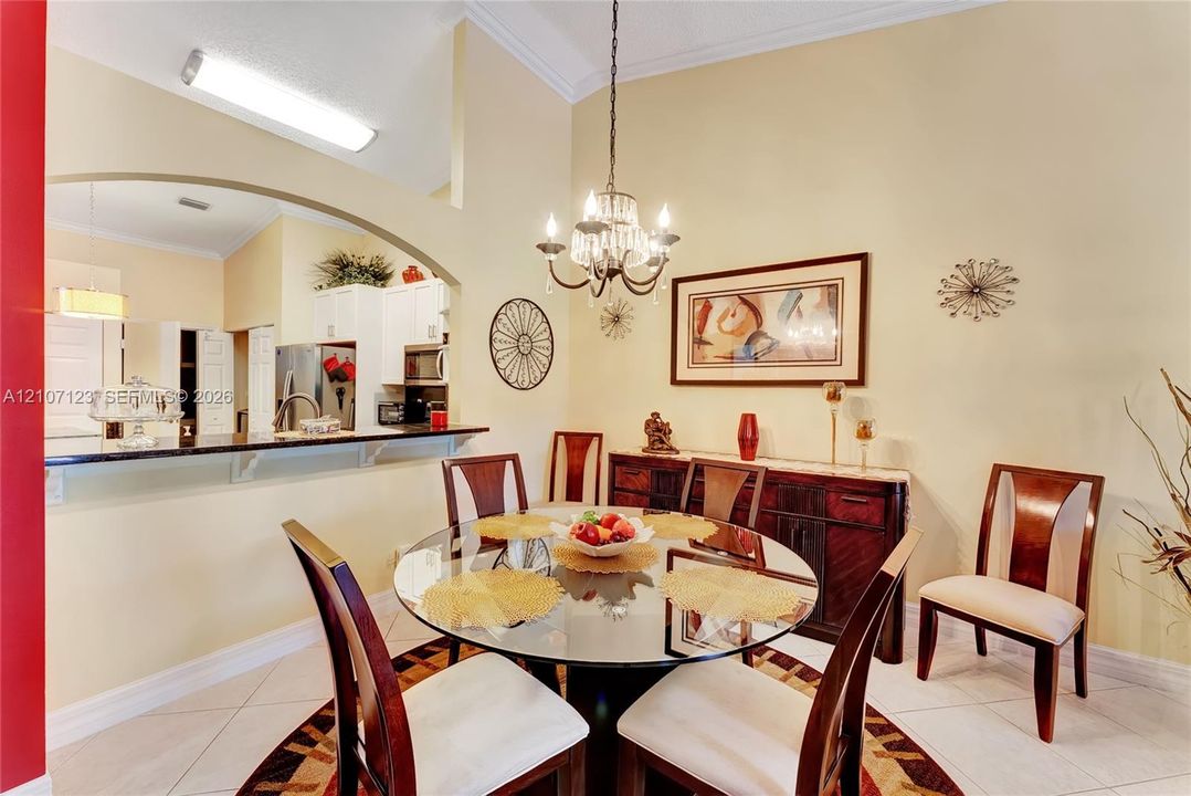 Dining area featuring vaulted ceilings, an arched wall opening, a decorative hanging chandelier, and neutral tile flooring