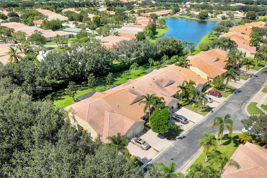 Aerial perspective featuring a tile roof, paved driveway, mature trees, and proximity to a community lake