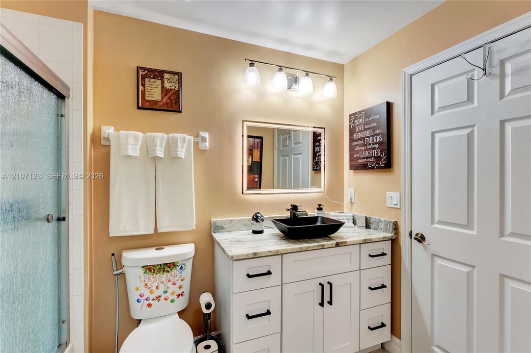 Bathroom vanity featuring white cabinetry, stone countertop, matte black hardware, and a rectangular vessel sink paired with an illuminated mirror