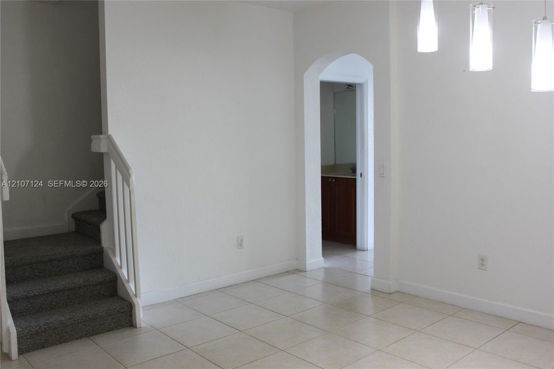Ceramic tile flooring, carpeted staircase with white baluster railing, arched doorway, and pendant light fixtures