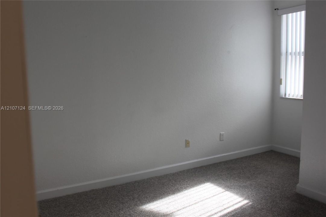 Neutral interior room featuring neutral-tone carpeting and vertical window blinds