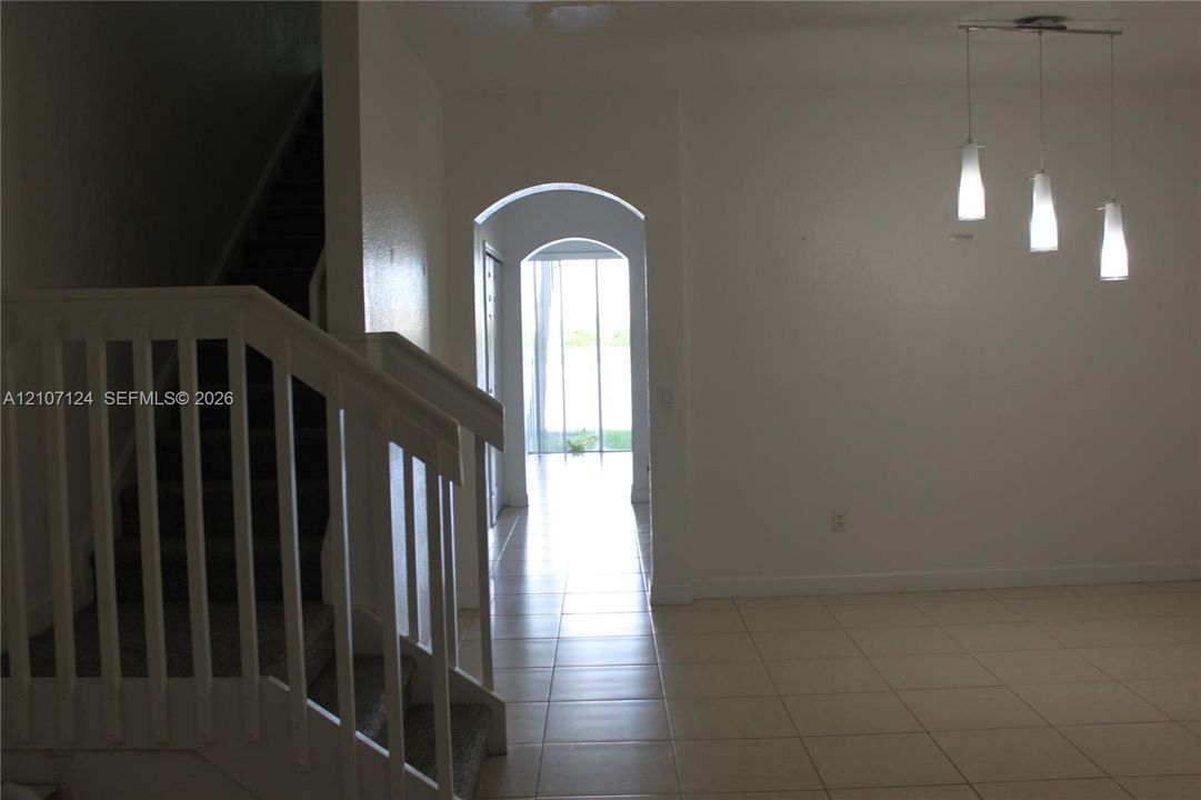 Interior space featuring large-format tile flooring, arched architectural pass-throughs, a staircase with white balusters, and a three-pendant light fixture