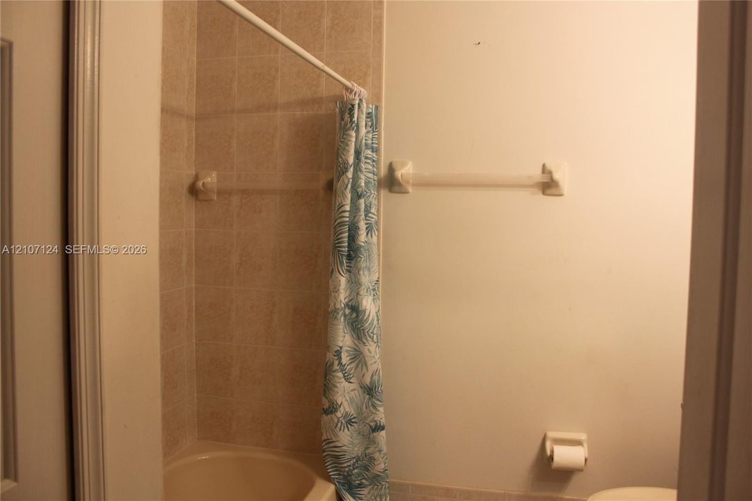 Bathroom featuring a shower stall with neutral tile surround, a built-in towel bar, and a wall-mounted toilet paper holder