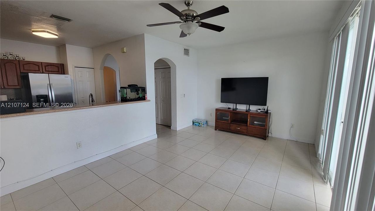 Open-concept interior featuring light-toned tile flooring, ceiling fan with integrated lighting, arched doorways, and sliding glass doors
