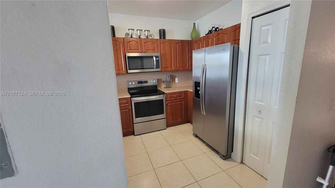 Kitchen featuring wood cabinetry, stainless steel appliances, tile flooring, and a pantry with a paneled door