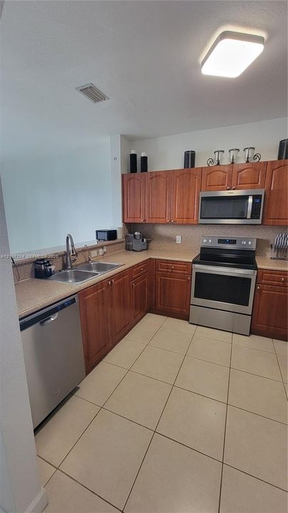Kitchen featuring wooden cabinetry, stainless steel appliances, solid-surface countertops, dual-basin sink with a high-arch faucet, and ceramic tile flooring