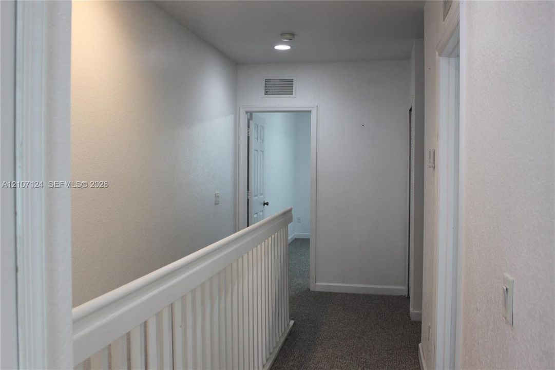 Hallway featuring carpeted flooring, a white wooden balustrade, and recessed ceiling lighting