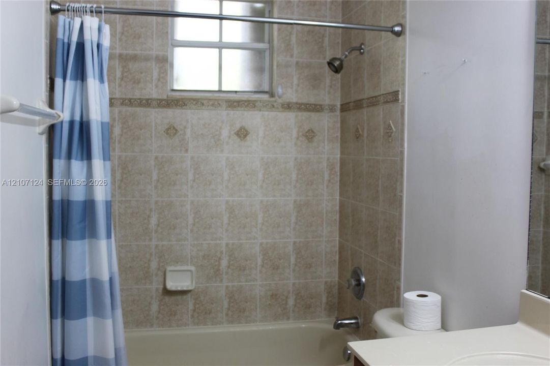 Full bathroom featuring a tub-shower combination, neutral ceramic wall tile with decorative accent detailing, a built-in soap dish, and a single-basin vanity with a countertop