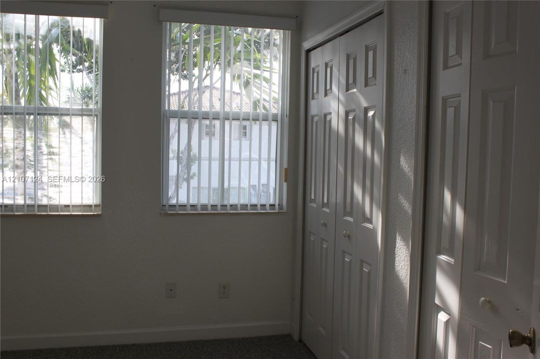 Dual windows with vertical blinds, neutral wall finish, and two sets of multi-panel bi-fold closet doors