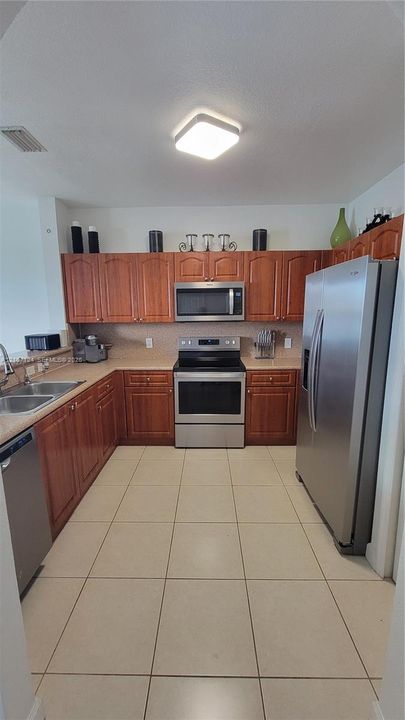 Kitchen featuring wood cabinetry, stainless steel appliances, neutral solid-surface countertops, and ceramic tile flooring