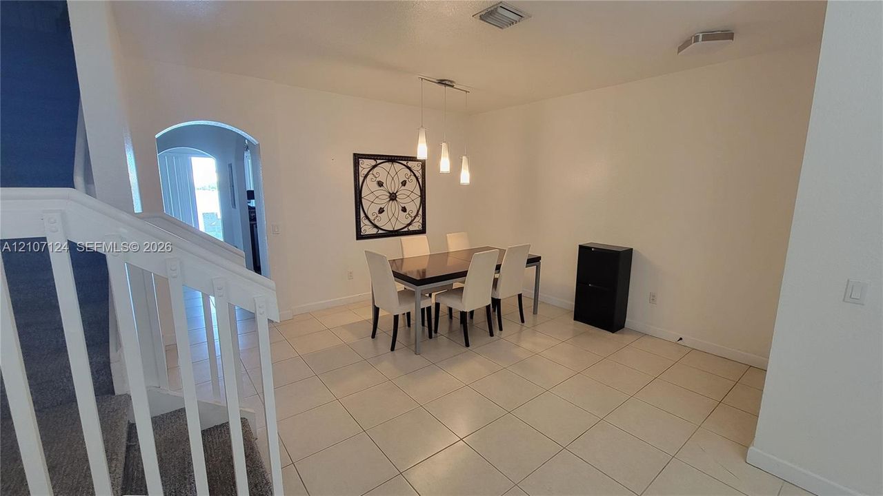 Open-concept space featuring ceramic tile flooring, a suspended three-light pendant fixture, and a decorative arched entryway