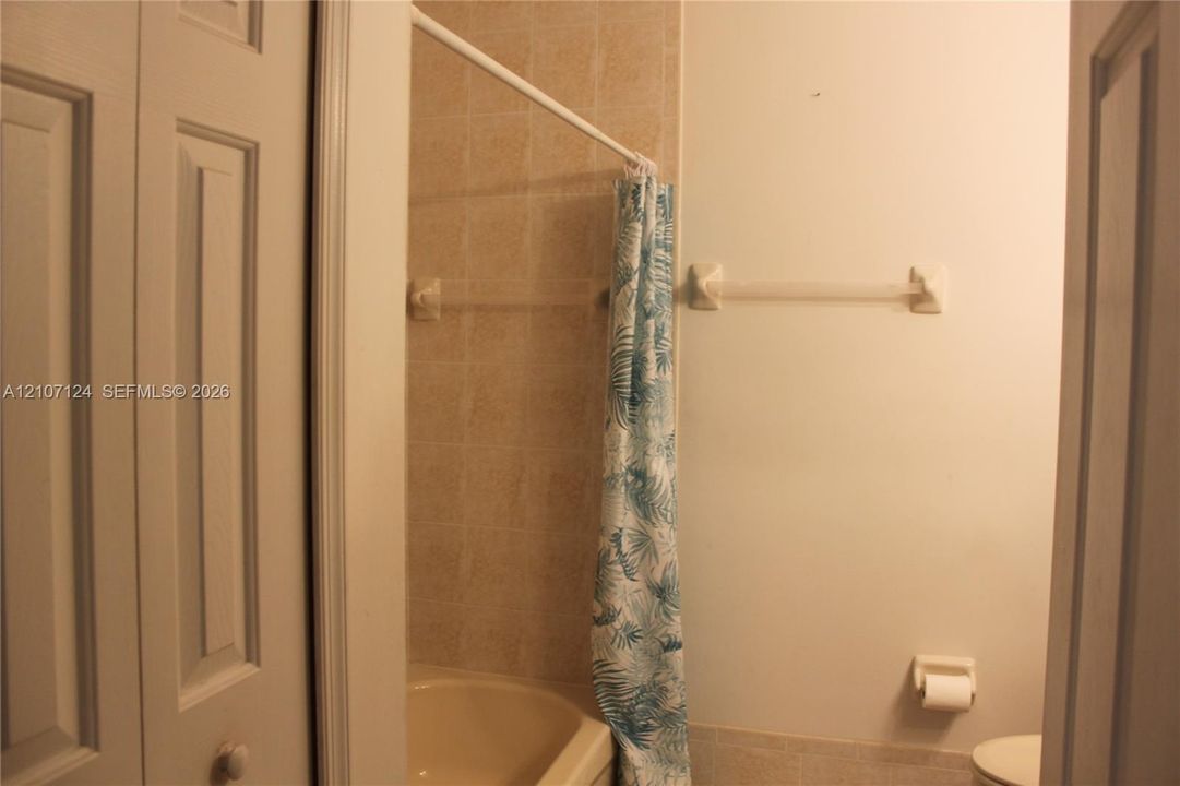 Bathroom featuring a tub with neutral-toned wall tiling, bifold closet doors, and a wall-mounted towel bar