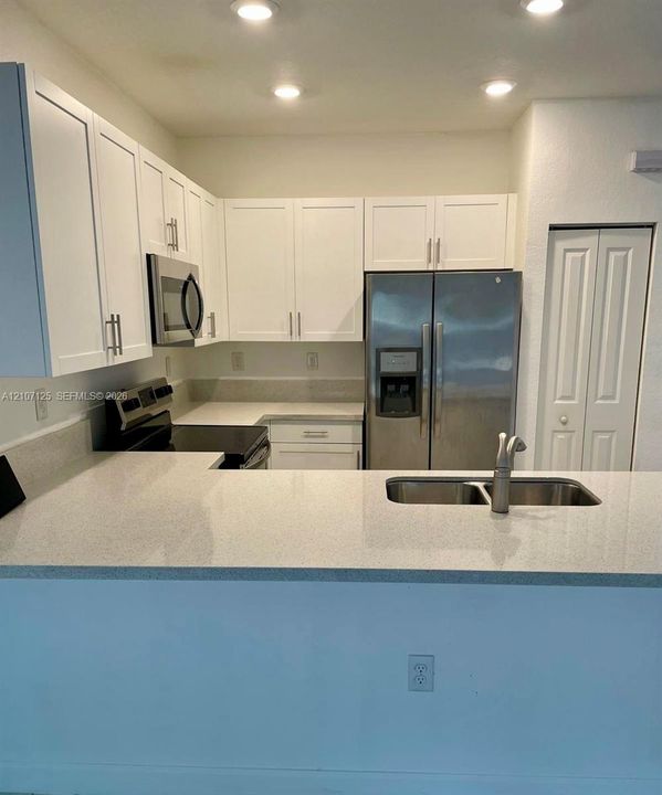 Kitchen featuring white shaker-style cabinetry, solid-surface countertops, recessed lighting, stainless steel appliances, and a dual-basin undermount sink