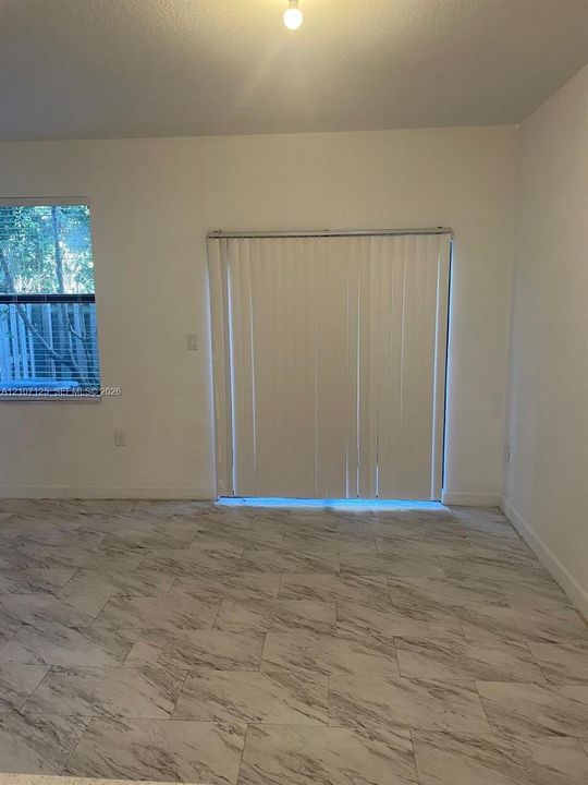 Neutral interior featuring large-format stone-patterned tile flooring, vertical window blinds, and natural light exposure