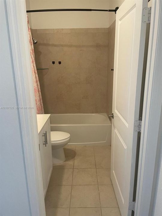 Bathroom featuring a tub-shower combination with tile surround, white vanity cabinet, tiled flooring, and a two-panel interior door