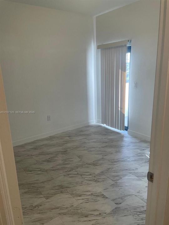 Neutral interior space featuring stone-finish tile flooring and vertical blinds