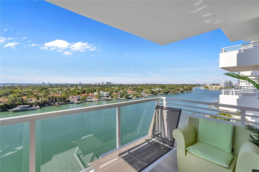 Private balcony featuring a glass-panel railing, metal frame, and tile flooring, oriented toward a water channel and coastal landscape