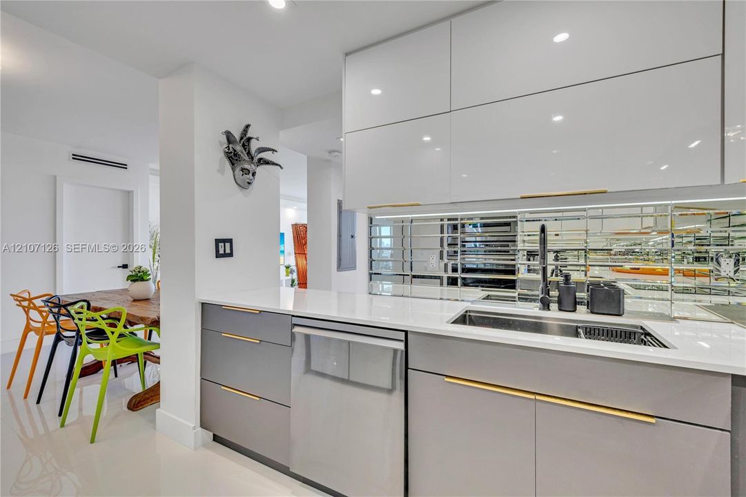 Kitchen featuring high-gloss cabinetry, stone countertops, mirrored tile backsplash, undermount sink with a matte black faucet, and brass-tone hardware