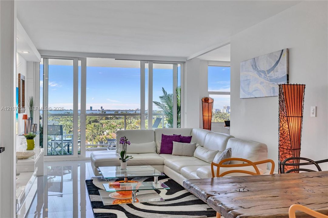 Open-concept interior featuring polished tile flooring, floor-to-ceiling glass sliding doors, and an attached balcony overlooking a coastal landscape