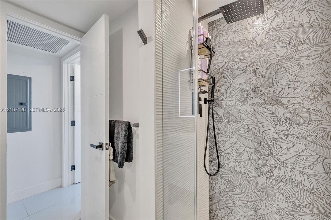Walk-in shower featuring a patterned tile wall, rainfall showerhead, glass enclosure, and matte black hardware