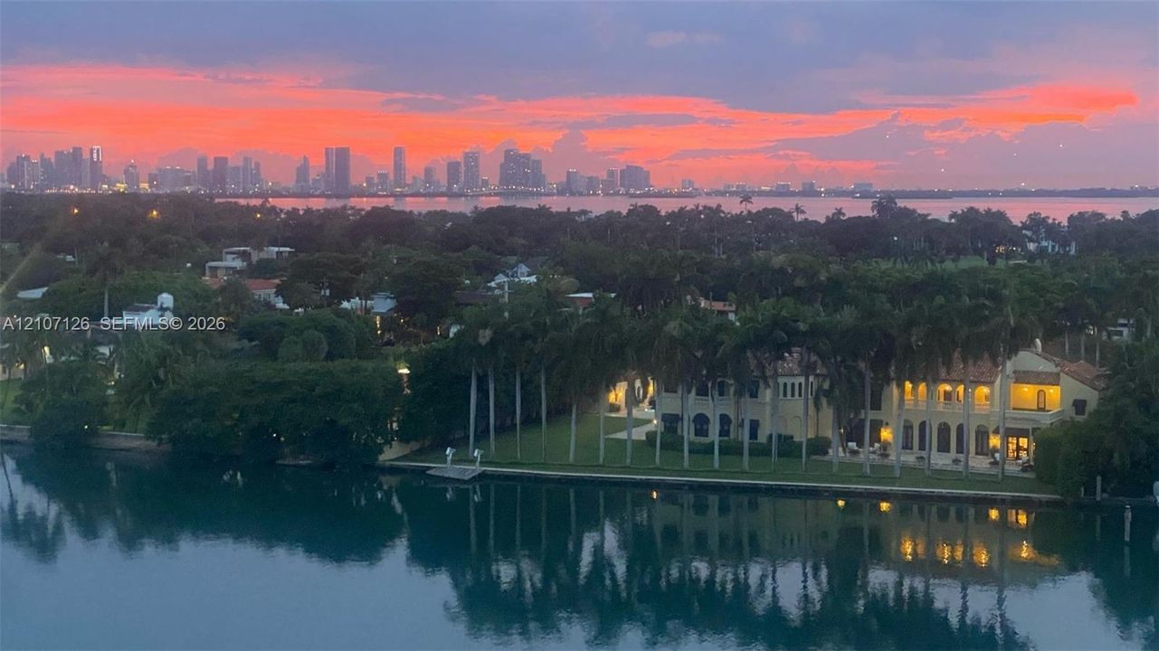 Waterfront estate featuring a multi-story residence, palm tree landscaping, direct bulkhead access to the water, and an expansive cityscape backdrop