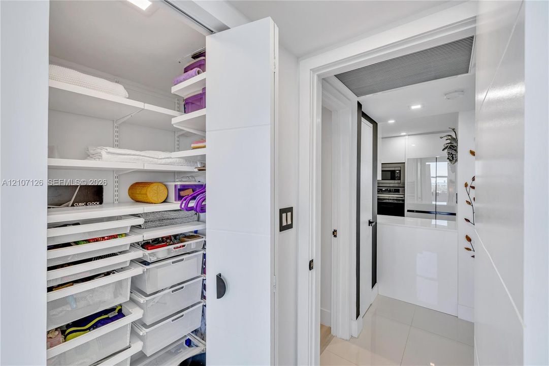 Built-in storage closet featuring adjustable shelving and integrated pull-out drawers, paired with large-format tile flooring and recessed ceiling lighting
