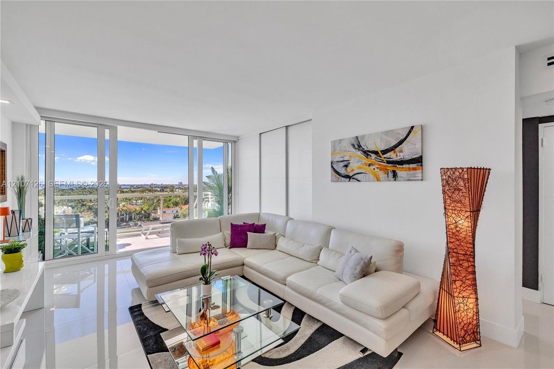 Living space featuring polished tile flooring, floor-to-ceiling glass sliding doors, and a private balcony with a glass railing