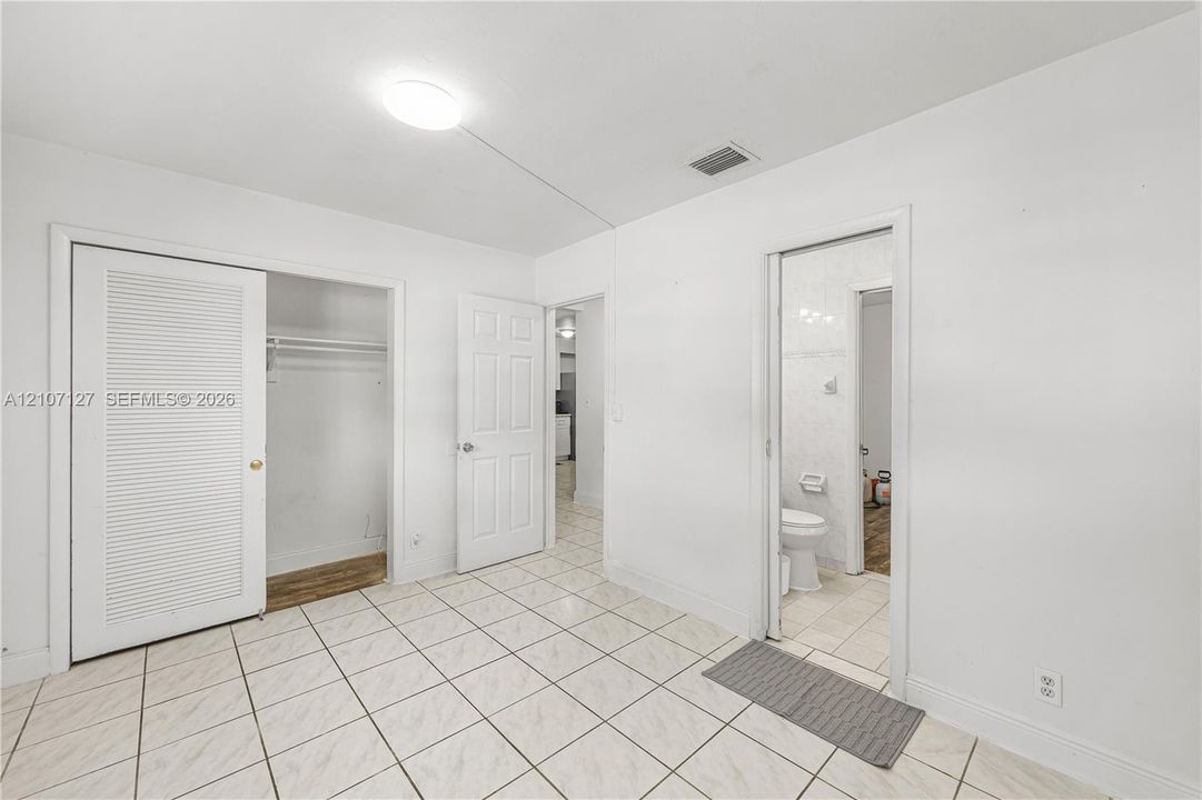 Ceramic tile flooring, closet with louvered bi-fold doors, six-panel interior door, and flush-mount ceiling lighting