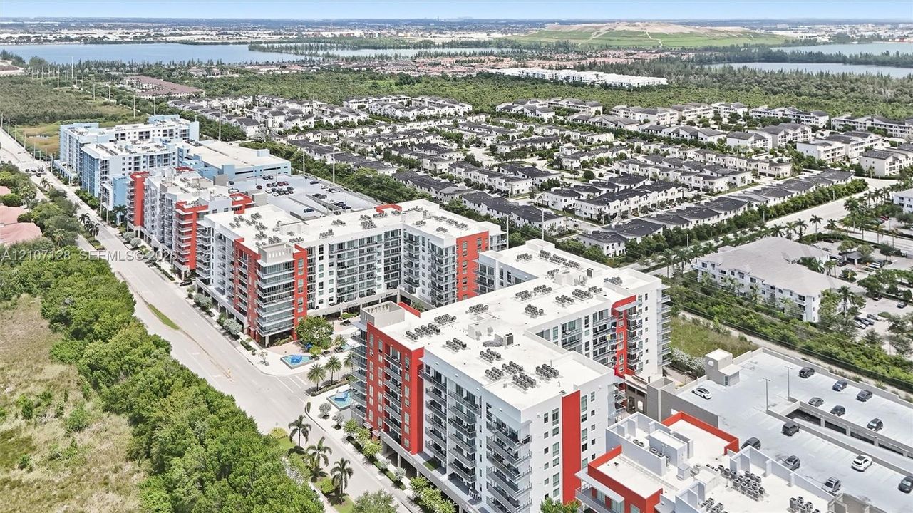 Aerial perspective of a multi-story residential complex featuring modern architecture, structured parking facilities, balcony units, and landscaped grounds