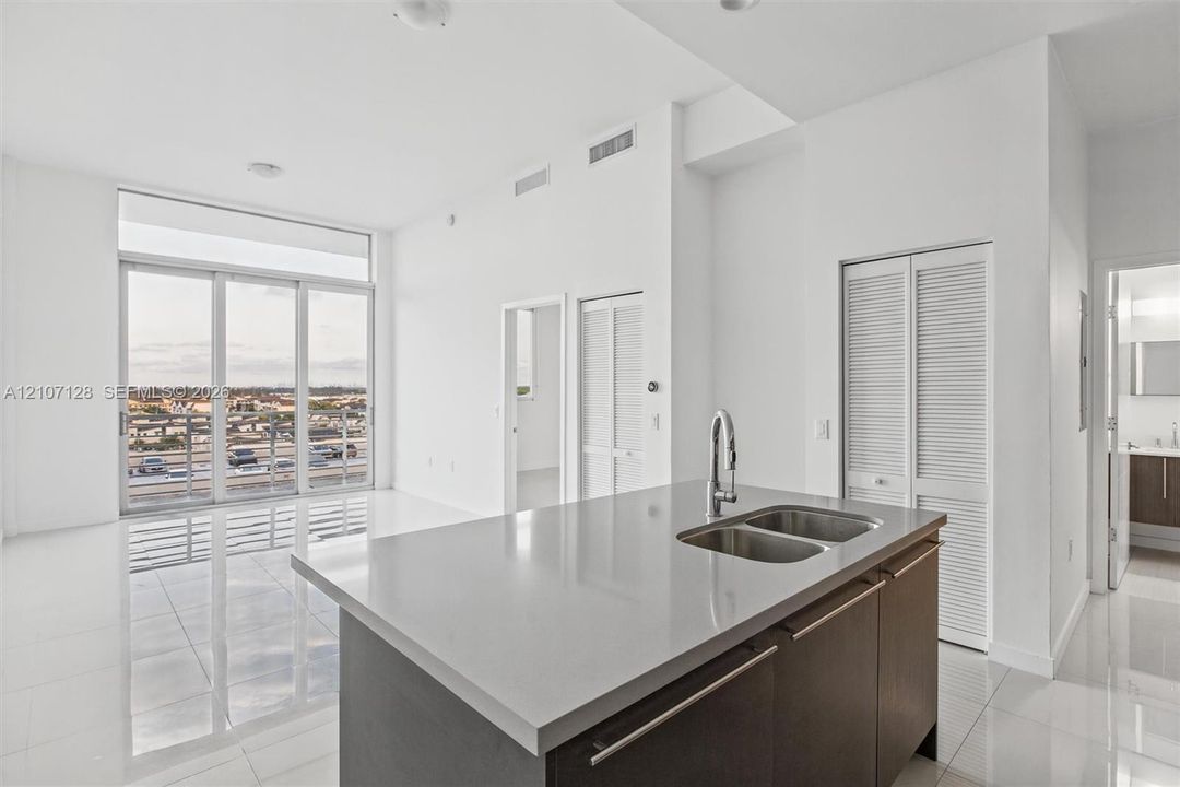 Open-concept kitchen featuring an island with a stone-composite countertop, dual-basin stainless steel sink, and high-arc faucet, complemented by floor-to-ceiling windows and polished tile flooring