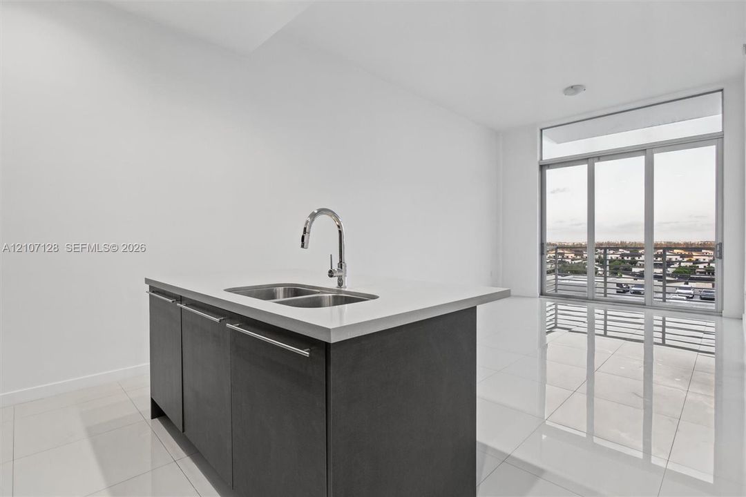 Center island featuring a stone countertop, dual-basin stainless steel sink, and high-arc chrome faucet, paired with dark cabinetry and polished tile flooring, highlighted by floor-to-ceiling glass sliding doors