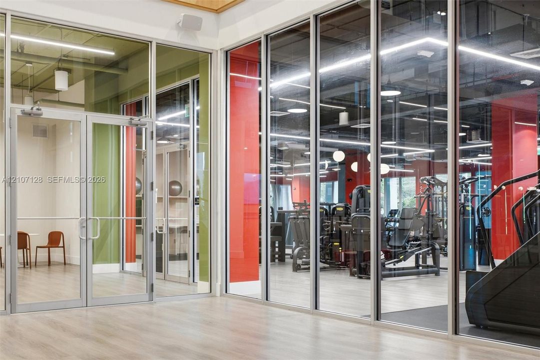 Floor-to-ceiling glass wall partitions with metal framing, wood-finish flooring, exposed ceiling elements, and recessed linear lighting