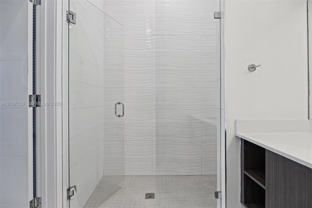 Walk-in shower featuring a frameless glass door, textured wave-pattern wall tile, mosaic floor tiling.