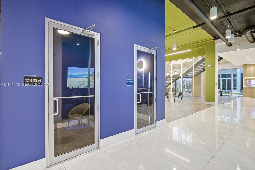 Enclosed glass-front rooms with polished tile flooring, contemporary color-blocked walls, exposed industrial-style ceilings, and pendant lighting