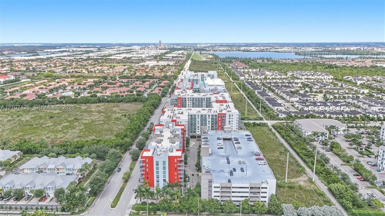 Aerial perspective featuring multi-story residential buildings with red and gray accents, integrated multi-level parking structure, and landscaped ground-level palms