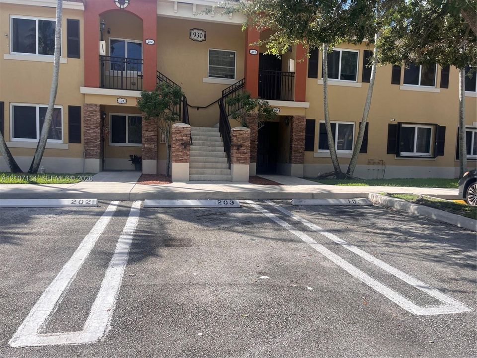 Two-story stucco exterior featuring stone veneer accents, decorative black shutters, metal railings, and reserved parking spaces