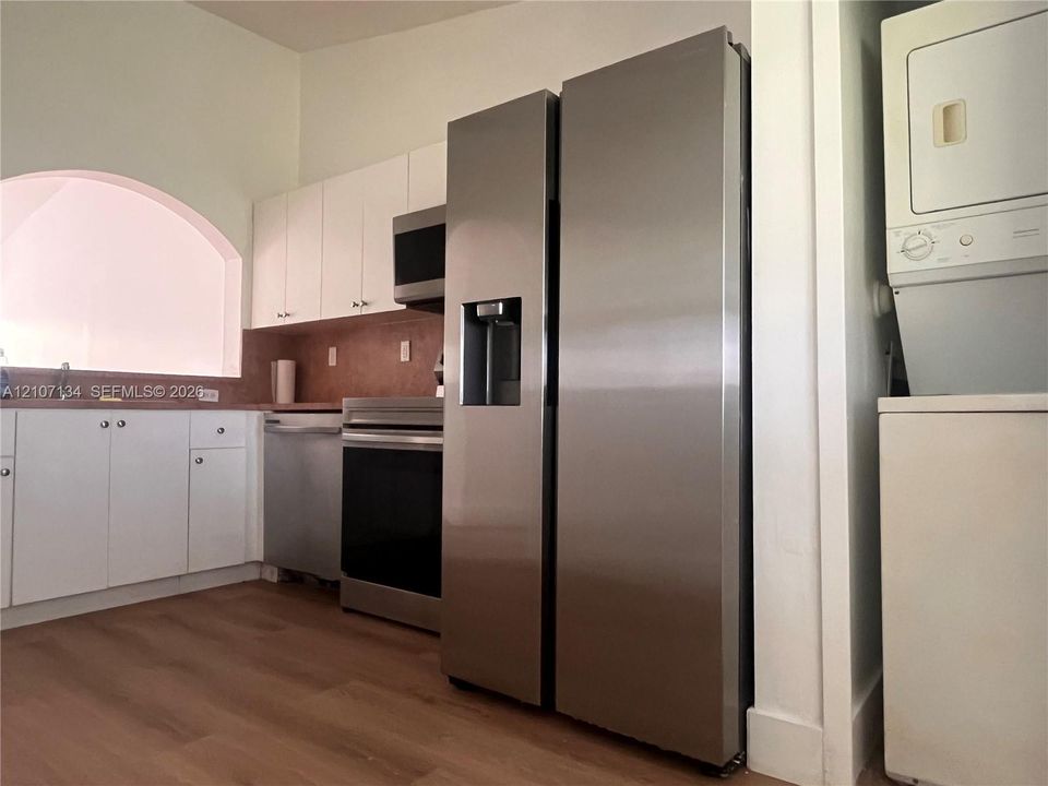 Kitchen featuring white cabinetry, stainless steel appliances, wood-finish flooring, a wall-mounted laundry unit, and an arched architectural opening
